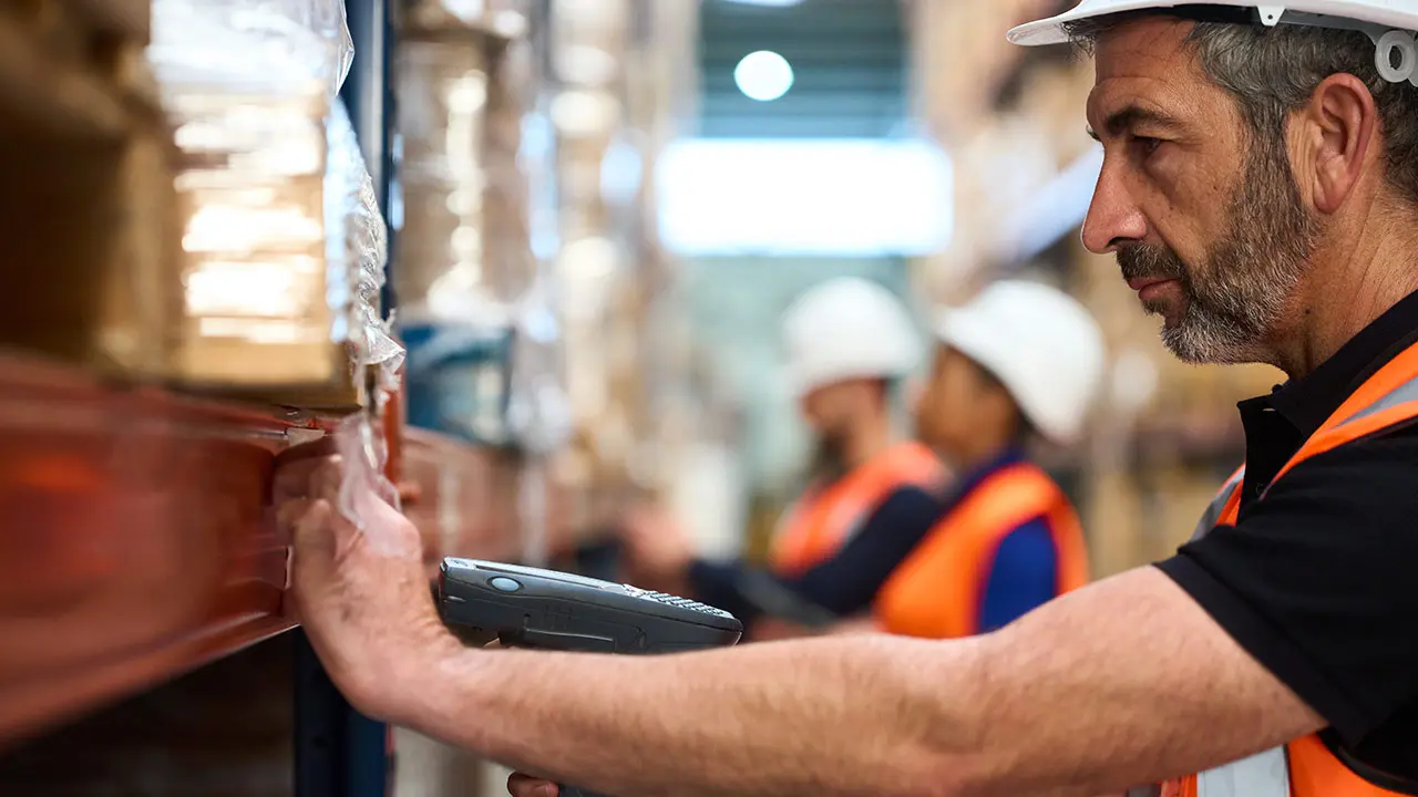 Operario logístico escaneando el etiquetado de estanterías de almacén durante el picking.