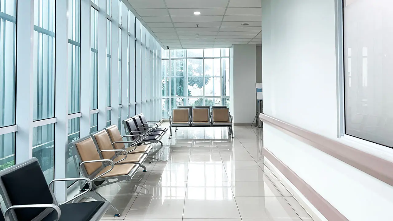 Interior de una clínica moderna con portacarteles de metacrilato y pantallas de gestión de turnos en la sala de espera.