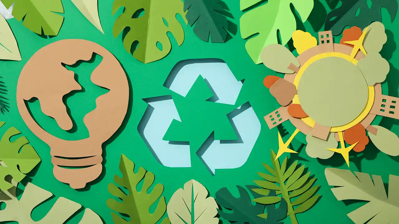Composición conceptual de ecodiseño en papel reciclado con símbolos de reciclaje, una bombilla y el planeta rodeados de hojas verdes.