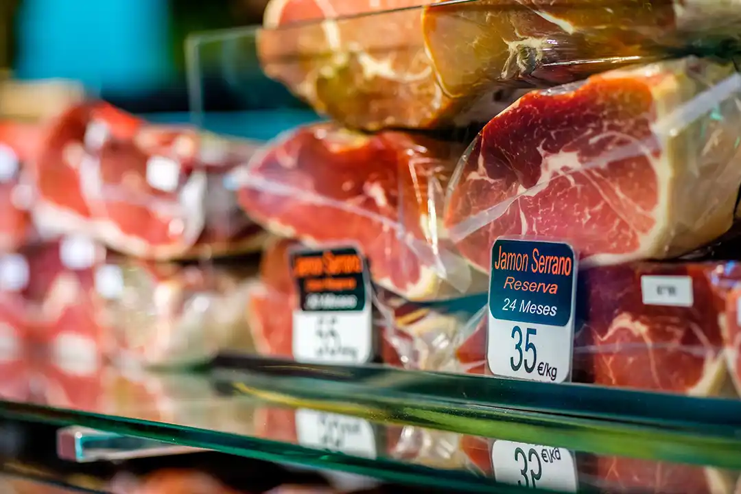Mostrador de charcutería con portaprecios negros unificados y corte de embutidos gourmet